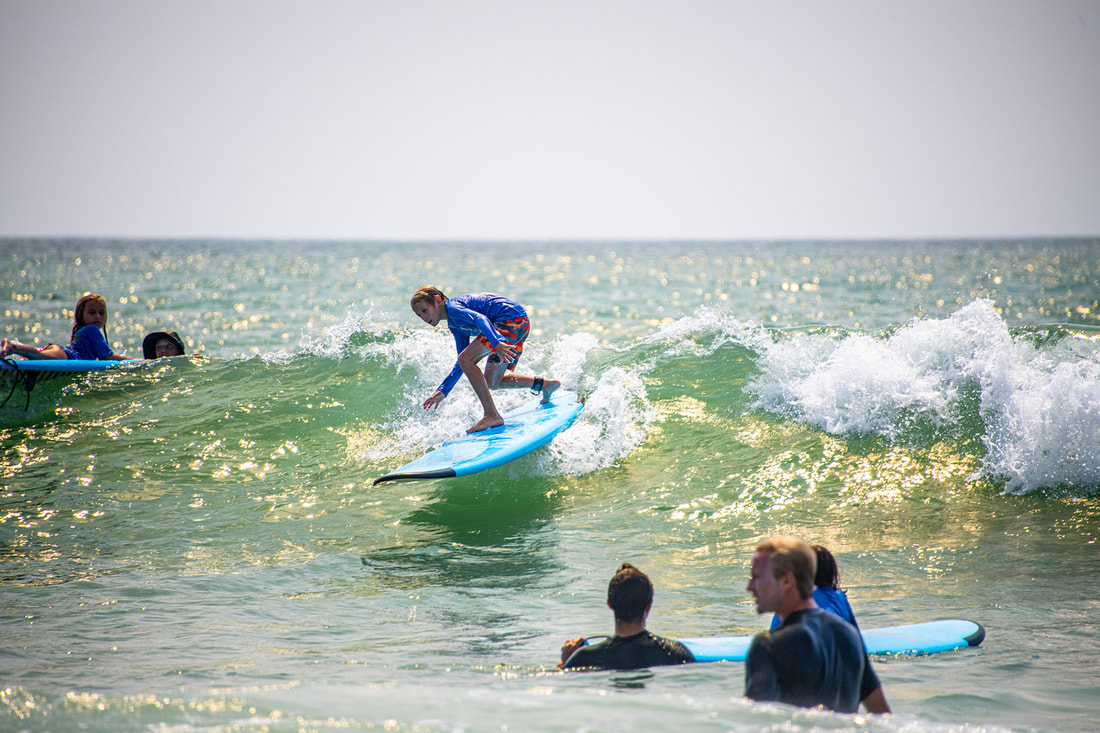 small girl surfs while instructor cheers