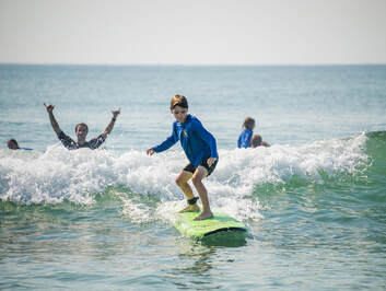 small girl surfs while instructor cheers